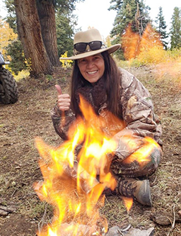 Suzanne standing in front of a campfire and giving a thumbs up
