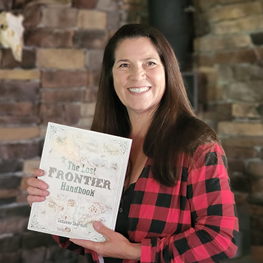 Suzanne smiling and showing the cover of The Lost Frontier Handbook